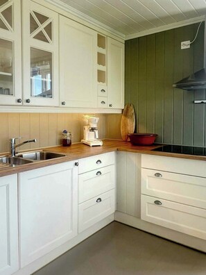 A kitchen with white cabinets, a wooden countertop, a coffee maker, and a red bowl.