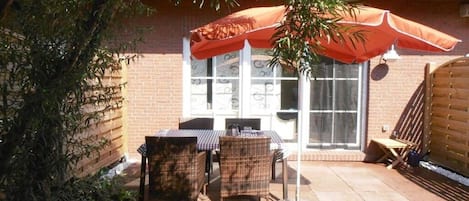 Eine Terrassenfläche mit Korbmöbeln, einem Tisch und einem Stuhl unter einem Sonnenschirm.
