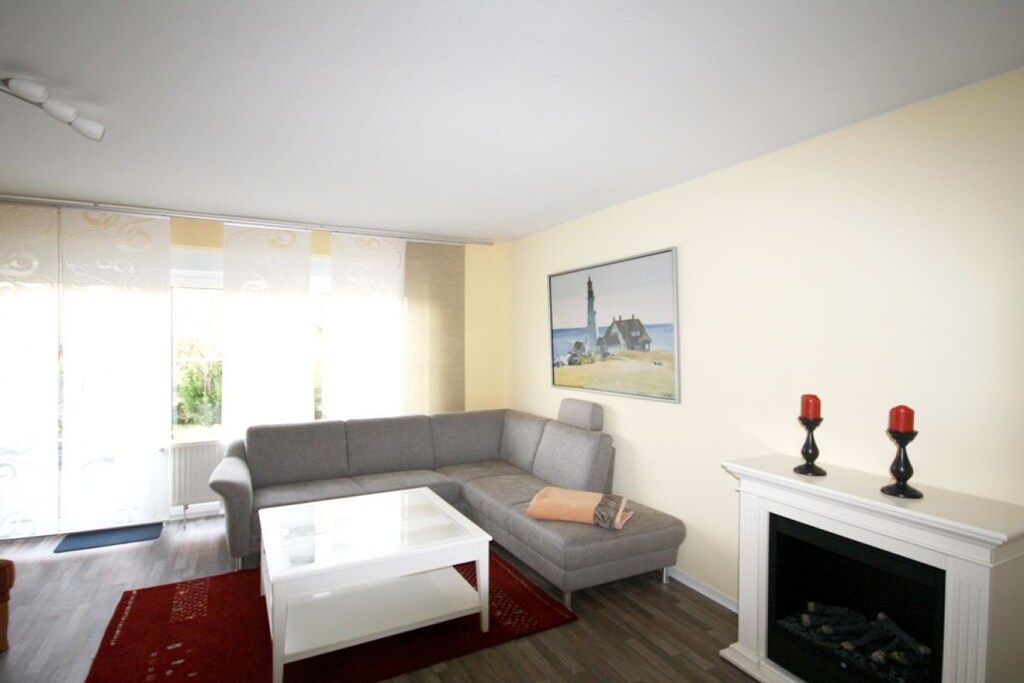 A living room with a grey sofa, a white coffee table, a fireplace with two red candles, and a painting of a lighthouse on the wall.