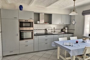 Een keuken met grijze kasten, een dubbele oven, een spoelbak en een eettafel met stoelen.