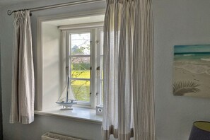 A room with a window, curtains, a small table with a decorative item, and a painting on the wall. - Holiday apartment with 2 bedrooms (Utersum auf Föhr)