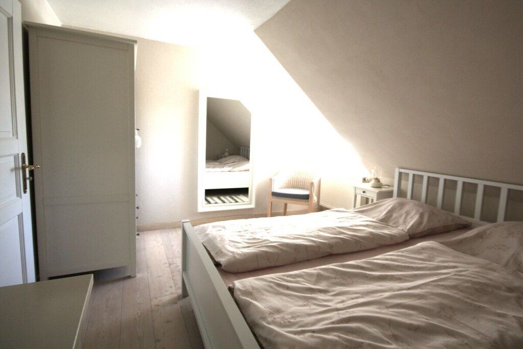 Une chambre avec un lit simple, une table de chevet, une chaise, une armoire et une fenêtre qui laisse entrer la lumière naturelle.
