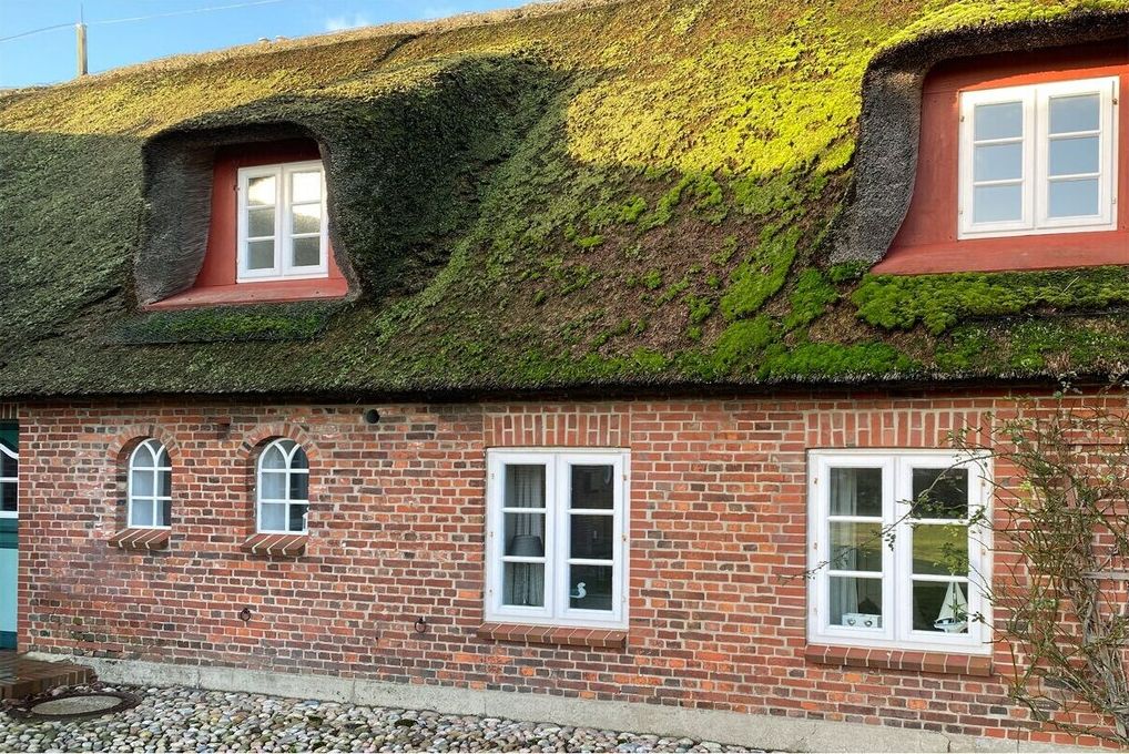 Ein traditionelles Backsteinhaus mit einem Strohdach und mehreren Fenstern.
