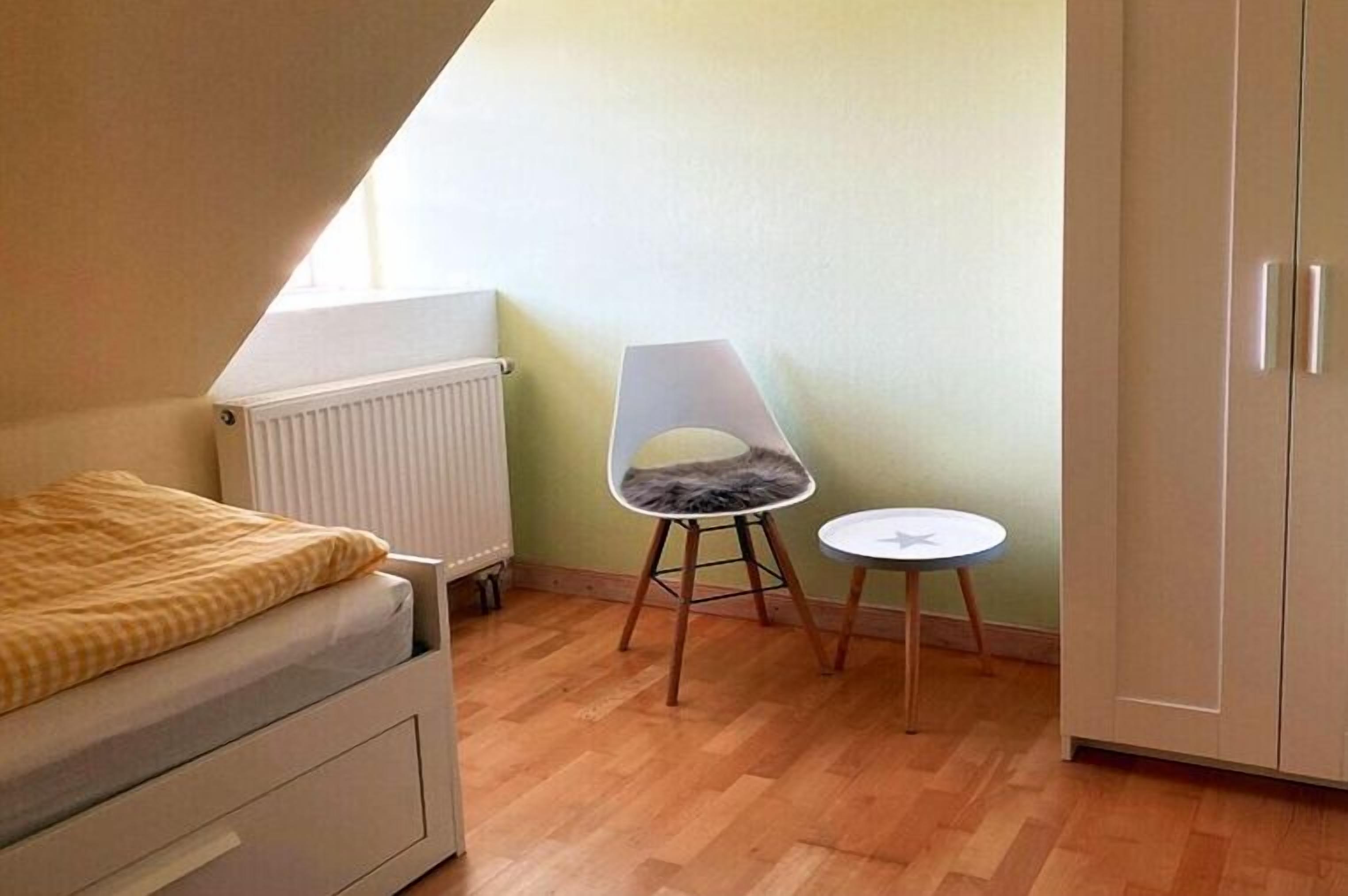 A small, single-room apartment with a bed, a radiator, a chair, a small table, and a wardrobe.
