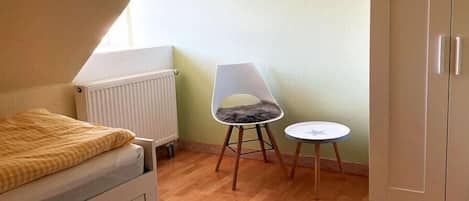 Un apartamento pequeño de una sola habitación con una cama, un radiador, una silla, una mesita y un armario.