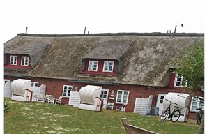 A traditional thatched-roof building with multiple rooms, each with a white door and a window. There are bicycles parked outside. - Holiday apartment with 2 bedrooms (Utersum auf Föhr)