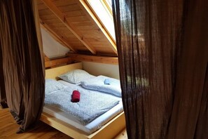 Ein Schlafzimmer im Loft-Stil mit schrägverdeckter Decke, Holzbalken und einem Bett mit Kissen und einem gerollten Handtuch.