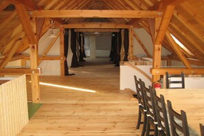 Quarto de sótão com vigas de madeira, uma mesa comprida e cadeiras.