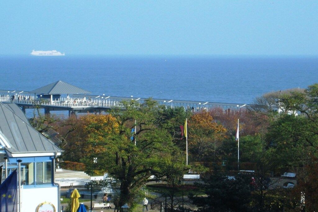 Blick auf die Küste mit einer Mole, die ins Meer führt, einer Flagge und einem Gebäude mit blauem Dach.