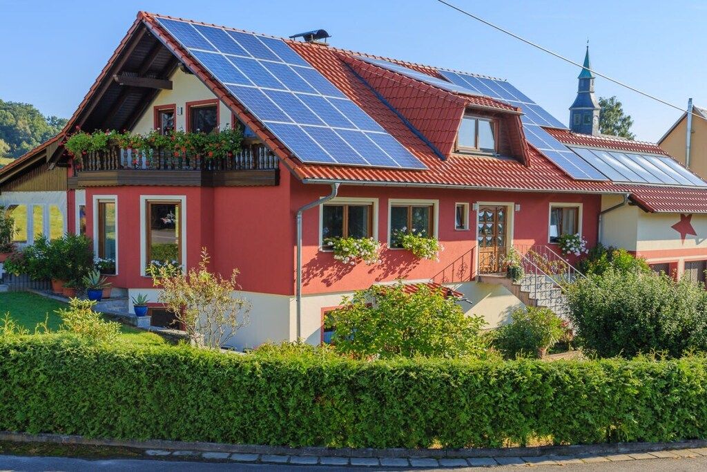 A house with solar panels, a red facade, and a traditional architectural style.