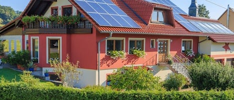 Una casa con paneles solares, fachada roja y estilo arquitectónico tradicional.
