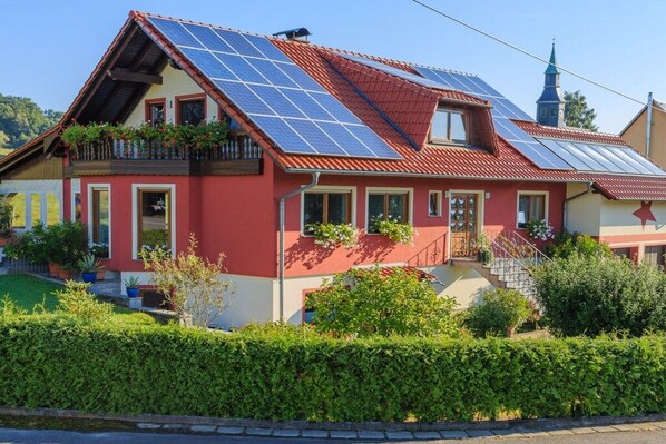 Una casa amb panells solars, façana vermella i estil arquitectònic tradicional.
