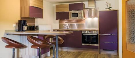 A modern kitchen with a bar area, stainless steel appliances, and a wooden floor.