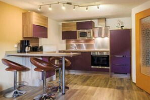 A modern kitchen with a bar area, stainless steel appliances, and a wooden floor. - Holiday apartment with 2 bedrooms (Hohnstein)