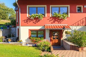 Una casa de dues plantes amb façana vermella, una porta d'entrada de fusta i una petita zona de porxo amb mobles d'exterior.