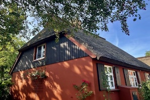 A traditional building with a thatched roof, wooden shutters, and a red facade. - Holiday home in Born with swimming pool (Born)