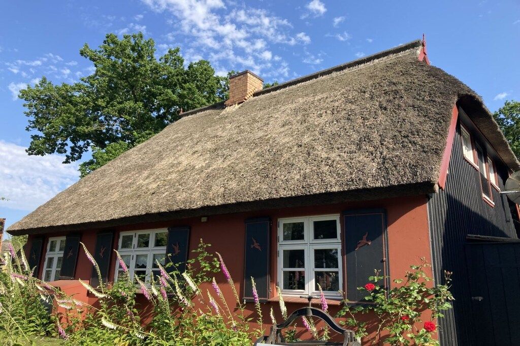 A traditional thatched-roof house with a red facade and white-framed windows.