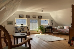 Ein gemütliches Dachzimmer mit Esstisch, Stühlen, einer Couch und einem großen Fenster.