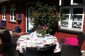 An outdoor dining area with a table set for two, surrounded by wicker chairs, and a potted plant with flowers. - Holiday home in Born with swimming pool (Born)