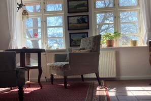 Ein Zimmer mit großem Fenster, einem Sessel, einem Tisch und einer Heizung.