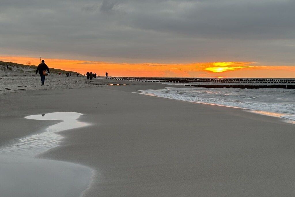 A beach with a sunset, a pier, and people walking.