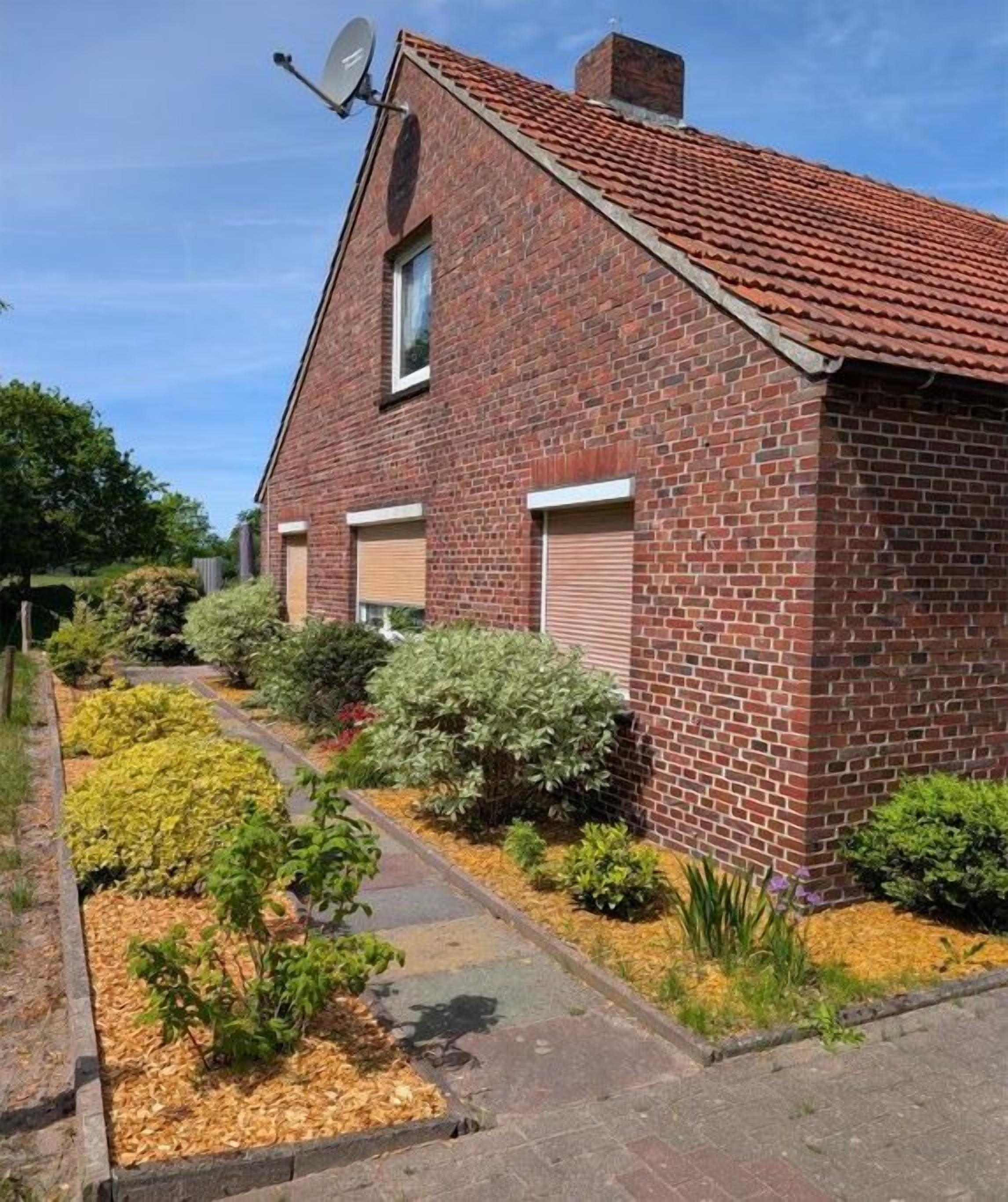 Een bakstenen huis met een schotelantenne, garage deuren en een tuin met verschillende planten.