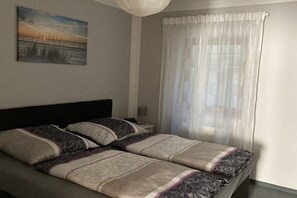 Een slaapkamer met een bed, kussens, een nachtkastje, een lamp en een schilderij aan de muur.
