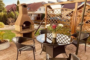 An outdoor patio with a stone-built pizza oven, wicker chairs, and a table with a vase of flowers. - Holiday apartment with 1 bedroom (Bannewitz)