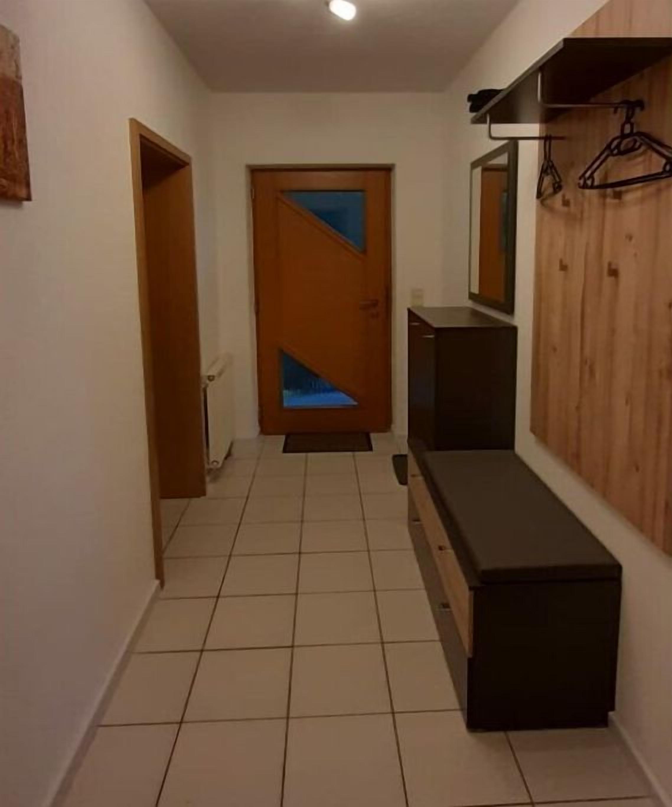 Un pasillo con puerta de madera, un banco y un espejo fijado a la pared.