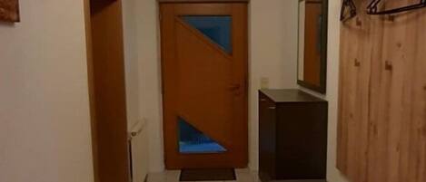 Un pasillo con puerta de madera, un banco y un espejo fijado a la pared.
