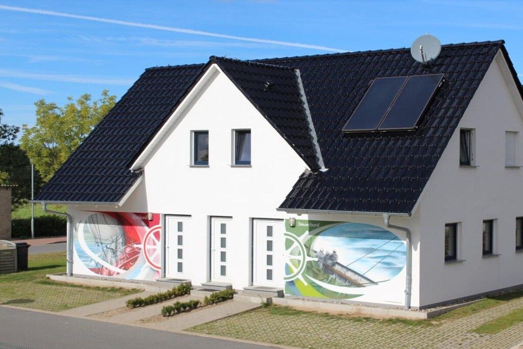 A modern two-story house with a sloped roof, solar panels, and a mural on the side.