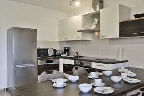 Eine moderne Küche mit Edelstahlgeräten, weißen Schränken und einem Essbereich mit einem dunklen Holztisch und weißen Stühlen.