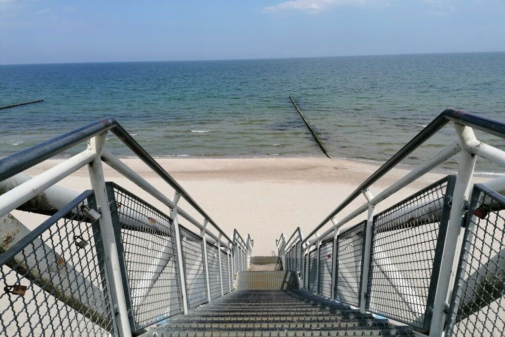 A set of metal stairs leading to a sandy beach with a view of the ocean.