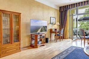 Ein Wohnzimmer mit einem Holzschrank, einem Flachbildfernseher, einem Tisch mit Stühlen und Blick durch eine Glastür.