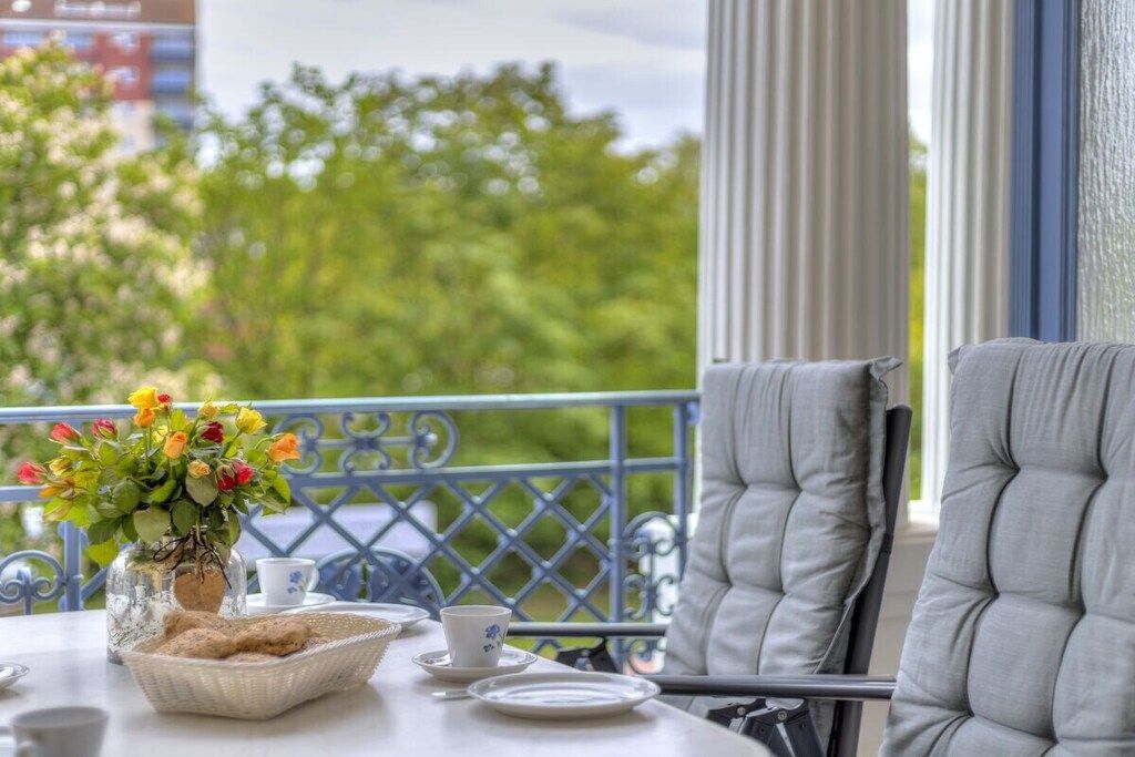 A balcony with a table set for two, a vase of flowers, and a view of trees.