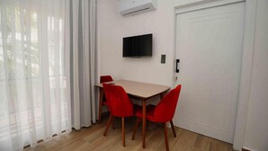 A room with a dining table, red chairs, a flat-screen TV, and an air conditioning unit. - Sofia Residence Apart Hotel (Çamyuva)