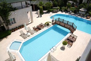 A swimming pool with a wooden bridge, lounge chairs, and a sun terrace.