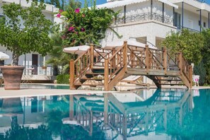 A pool area with a wooden bridge, potted plants, and a building with balconies. - Sofia Residence Apart Hotel (Çamyuva)