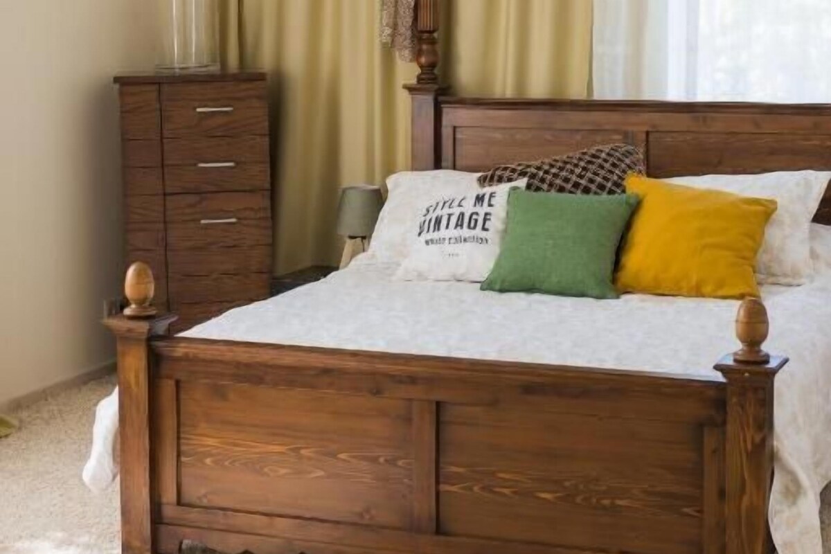 A bedroom with a wooden bed, a nightstand, a lamp, and a window with curtains.