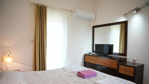 A hotel room with a bed, a dresser, a television, and an air conditioning unit. - Sofia Residence Apart Hotel (Çamyuva)