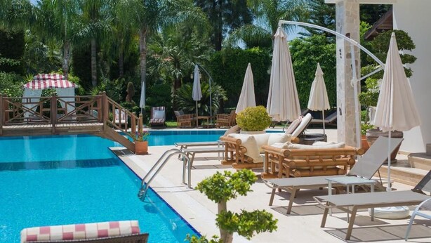A poolside area with lounge chairs, umbrellas, and a wooden deck. - Sofia Residence Apart Hotel (Çamyuva)