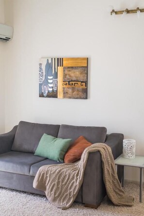 A modern living room with a grey sofa, a throw blanket, and a decorative wall piece.