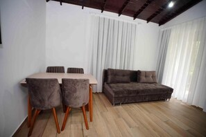A room with a wooden floor, a dining table with four chairs, and a brown sofa. - Sofia Residence Apart Hotel (Çamyuva)