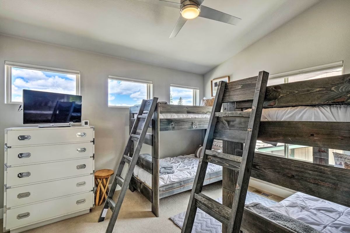 A bedroom with bunk beds, a TV, a dresser, and windows.