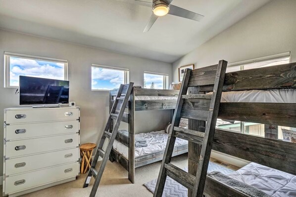 A bedroom with bunk beds, a TV, a dresser, and windows.
