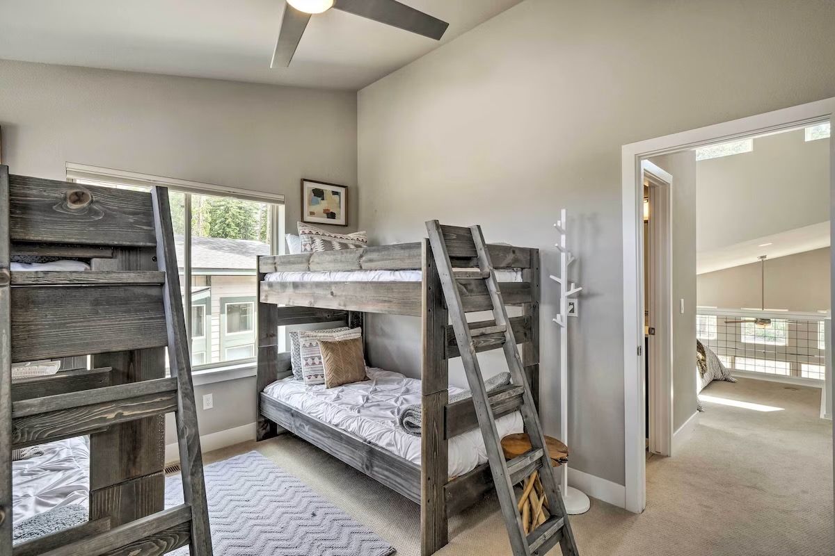 A bunk bed room with a ladder, a window, and a door leading to another room.