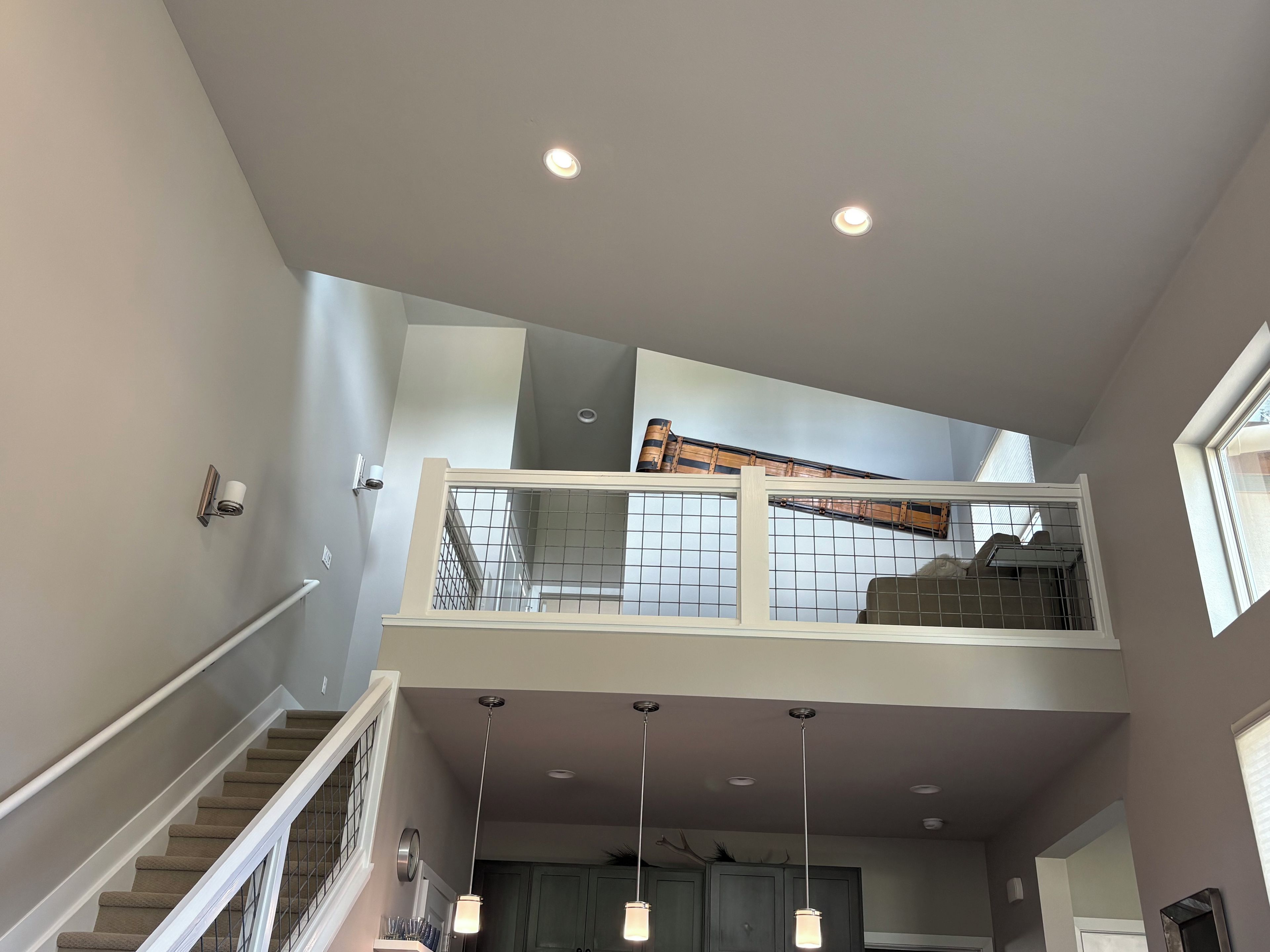 Un intérieur à plusieurs niveaux, avec un escalier, un balcon doté d’une balustrade et un éclairage suspendu.