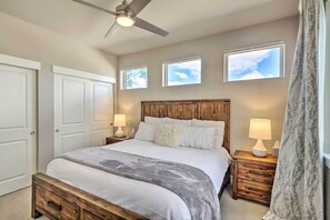 A bedroom with a bed, two bedside tables, a ceiling fan, and three windows.
