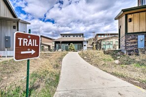 A trail sign pointing to the right, a concrete path, and modern buildings with a clear sky.