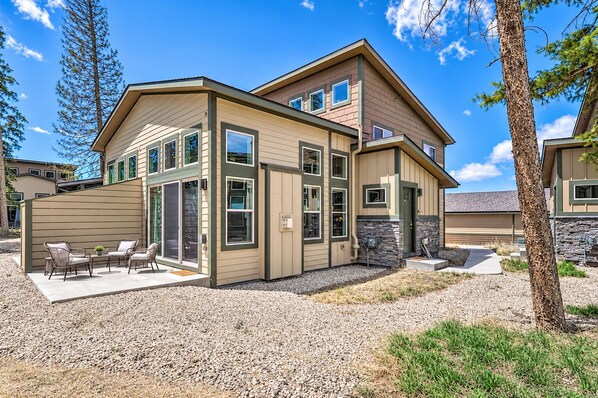 A modern two-story house with a covered patio area, large windows, and a stone foundation.